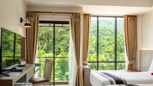 A hotel room with a desk, two beds, a chair, and large windows offering a view of a forest. - Ozone Hotel Khao Yai (Pak Chong)