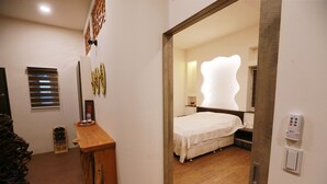 A hotel room with a wooden desk, a bed with a white bedspread, a wall-mounted light fixture, and a small wine rack. - Water Tail Homestay (Puli)