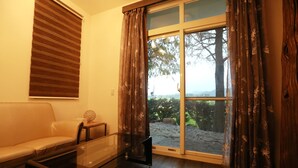 A room with a sofa, a glass coffee table, a wooden floor, and a sliding glass door leading to an outdoor area with a view of trees and mountains. - Water Tail Homestay (Puli)