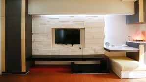 A modern living room with a flat-screen TV mounted on a white brick wall, a black entertainment unit, and a small seating area with a red accent wall. - Water Tail Homestay (Puli)