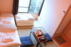 Ein Zimmer mit zwei Betten, einem kleinen Tisch mit Teezubehör und Blick auf Bäume durch ein Fenster.