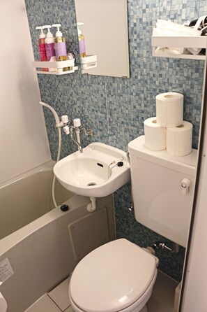 Ein kleines Badezimmer mit Waschbecken, Toilette und Badewanne. Über dem Waschbecken befindet sich ein Ablageschrank mit Pflegeprodukten.