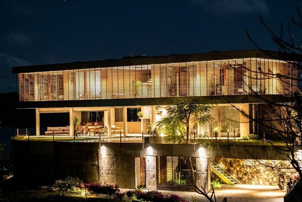 A modern two-story house with a large glass facade, a visible outdoor seating area, and a swimming pool. - Villa Strata (Kuta)