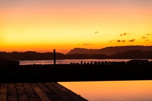 A sunset view from a wooden deck overlooking a body of water with distant mountains. - Villa Strata (Kuta)