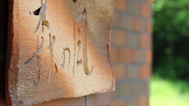 Un muro de ladrillo con una placa de madera que muestra figuras talladas y texto.