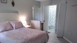 Ett sovrum med en säng, ett sängbord med en lampa, en spegel och ett badrum som syns genom en öppen dörr.