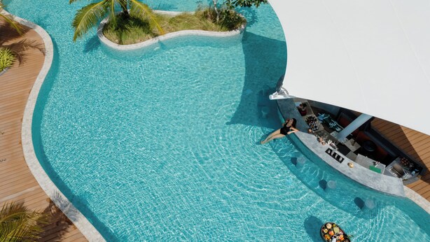 Luchtbeeld van een resort zwembad met een houten terras, ligstoelen en een bar.