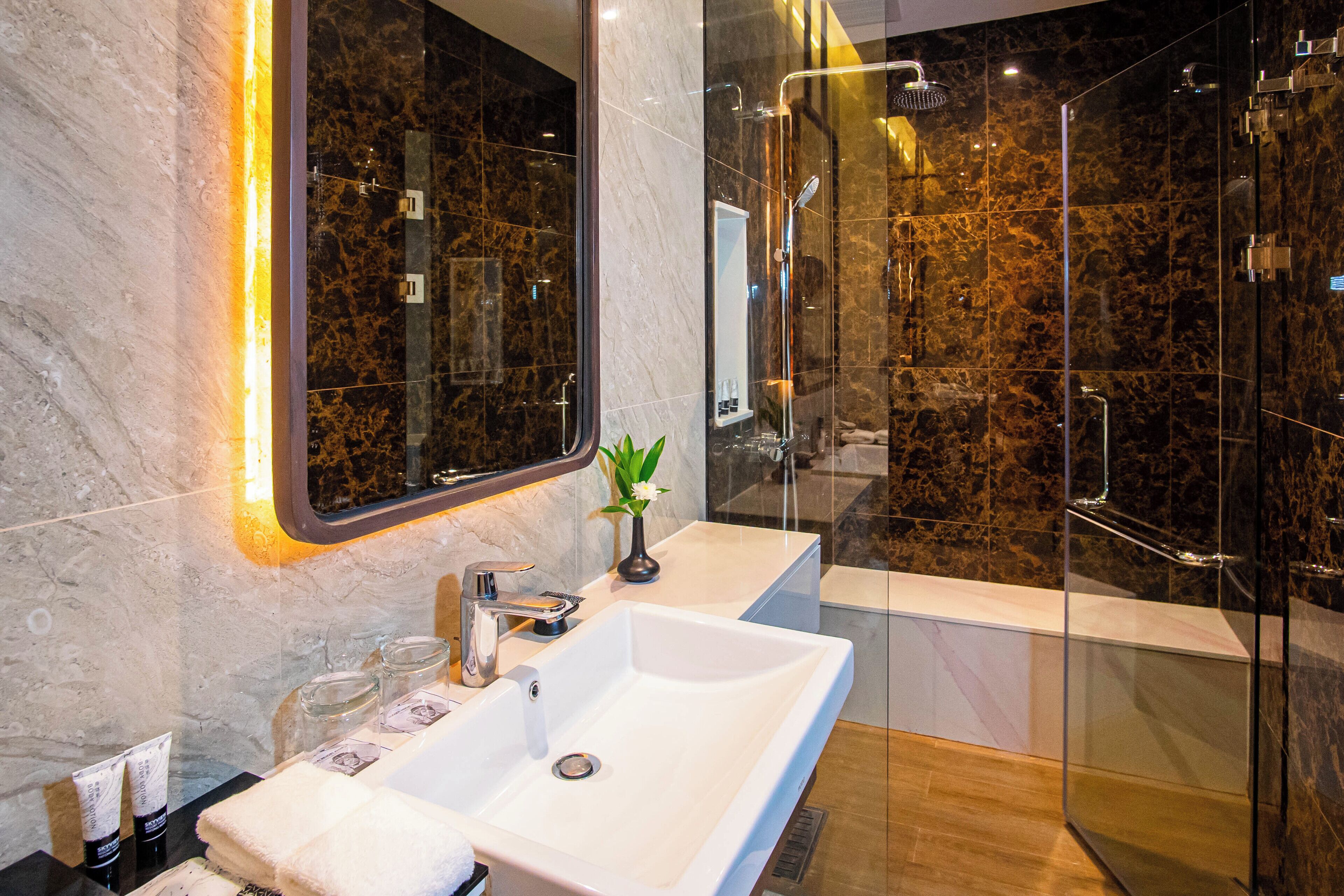 A modern bathroom with a white sink, a glass shower enclosure, and a marble-tiled wall.