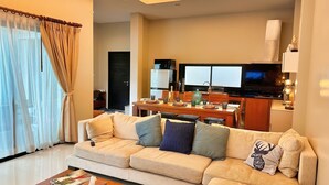 A modern living room with a sofa, coffee table, and a dining area with a TV and kitchen appliances.