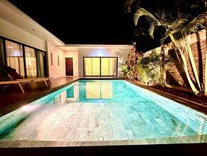 En swimmingpool med en kakelbeklädd poolkant, en dörr och ett fönster med gardiner.