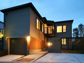 Ein modernes, zweistöckiges Haus mit Garage, einer Holzterrasse und einem umzäunten Garten.