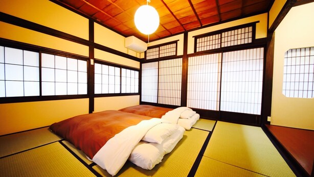 A traditional Japanese room with tatami mats, a futon bed, sliding shoji doors, and a hanging light fixture. - Utatei Takayama (Takayama)