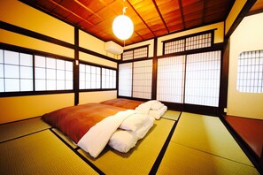 Ein traditioneller japanischer Raum mit Tatami-Matten, einer Futon-Liege, verschiebbaren Shoji-Türen und einer hängenden Leuchte.