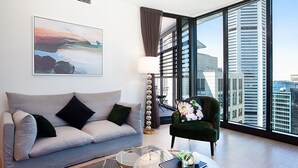 A modern living room with a grey sofa, a green armchair, and a large window offering a city view.