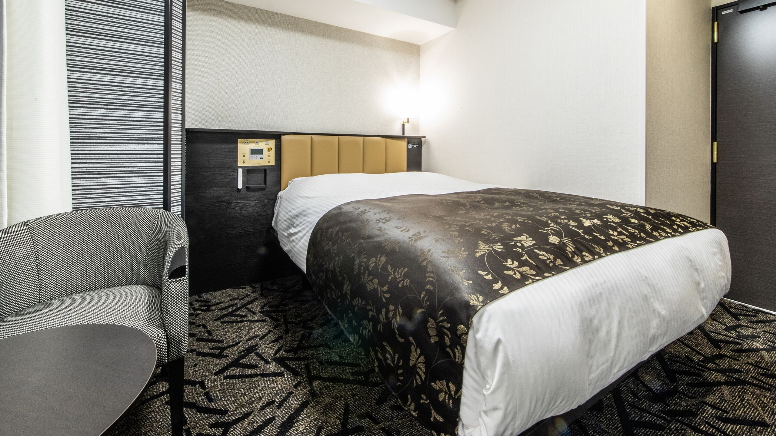 Una habitación de hotel con una cama, una silla, un escritorio y un panel de control en la pared.