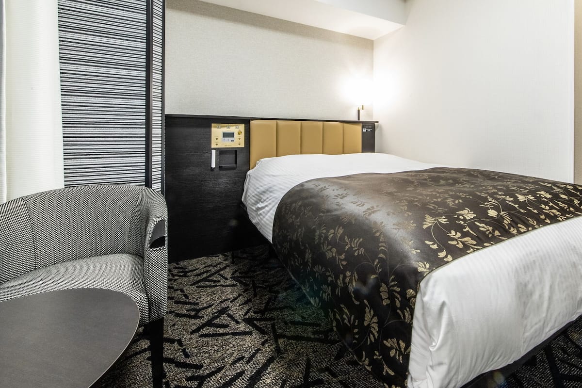Une chambre d’hôtel équipée d’un lit, d’une chaise, d’un bureau et d’un panneau de commande fixé au mur.