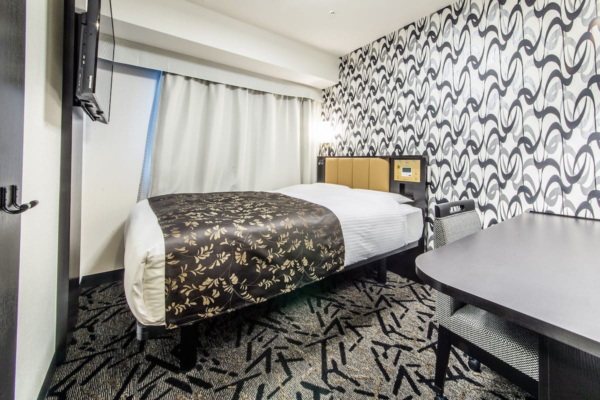 Une chambre d’hôtel avec un lit, un bureau, une chaise et un mur décoré de motifs.