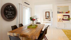Ein Essbereich mit einem Holztisch, Stühlen und einer Vase mit Blumen. An der Wand hängt ein Schild und es steht eine weiße Kommode mit Büchern darin.