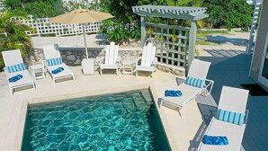 Ein Poolbereich mit klarem Wasser, weißen Liegestühlen mit blauen Kissen und einer Pergola.