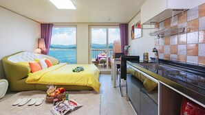 Ein kompaktes Hotelzimmer mit Bett, Küchenzeile und einem Balkon mit Meerblick.