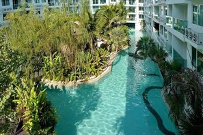A pool surrounded by lush greenery and a multi-story building with balconies. - Amazon Residence Jomtien Pattaya By New (Pattaya)