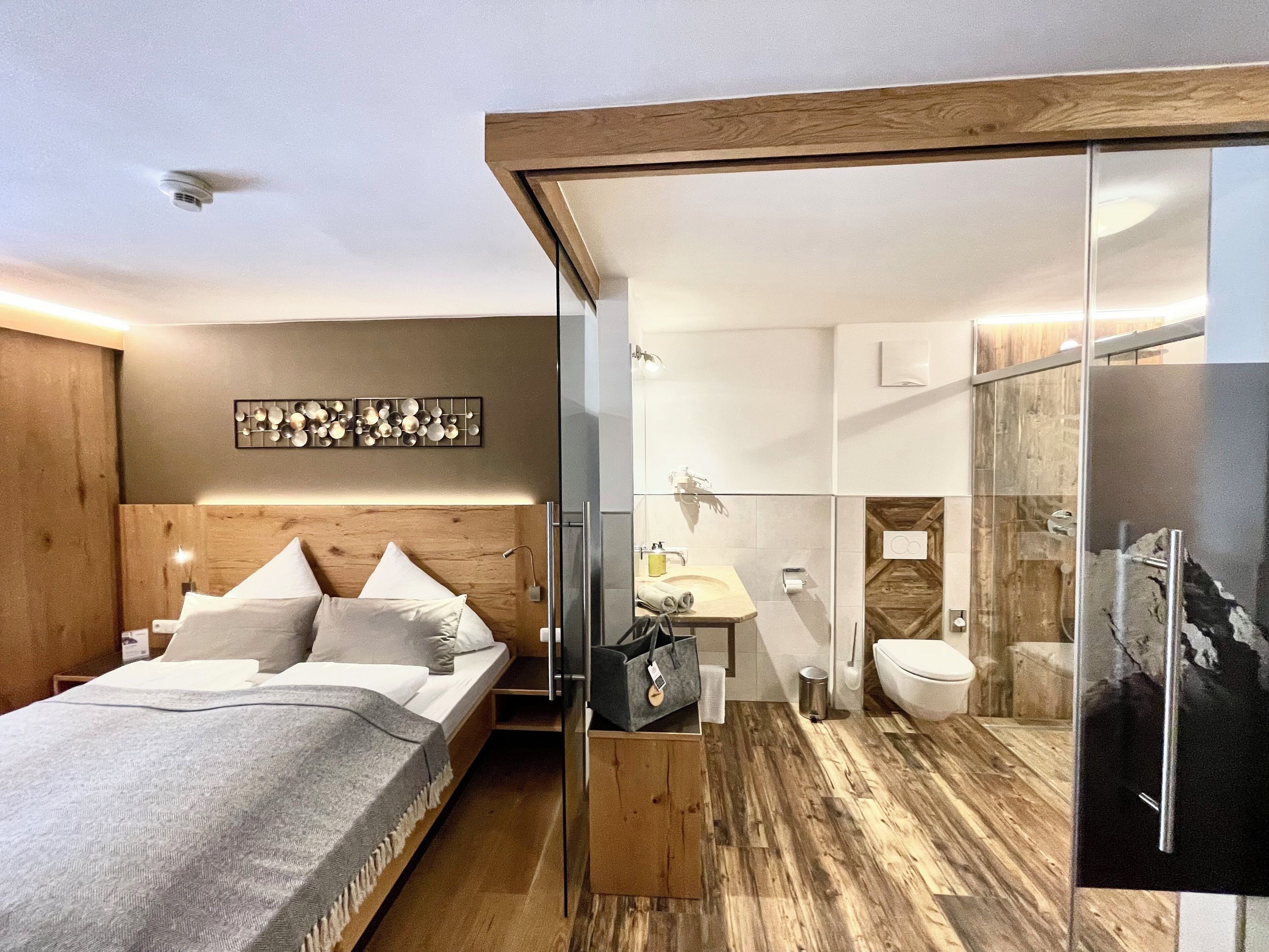 Quarto moderno com cabeceira de madeira, cama com lençóis brancos, mesa de cabeceira com abajur e uma obra de arte na parede.