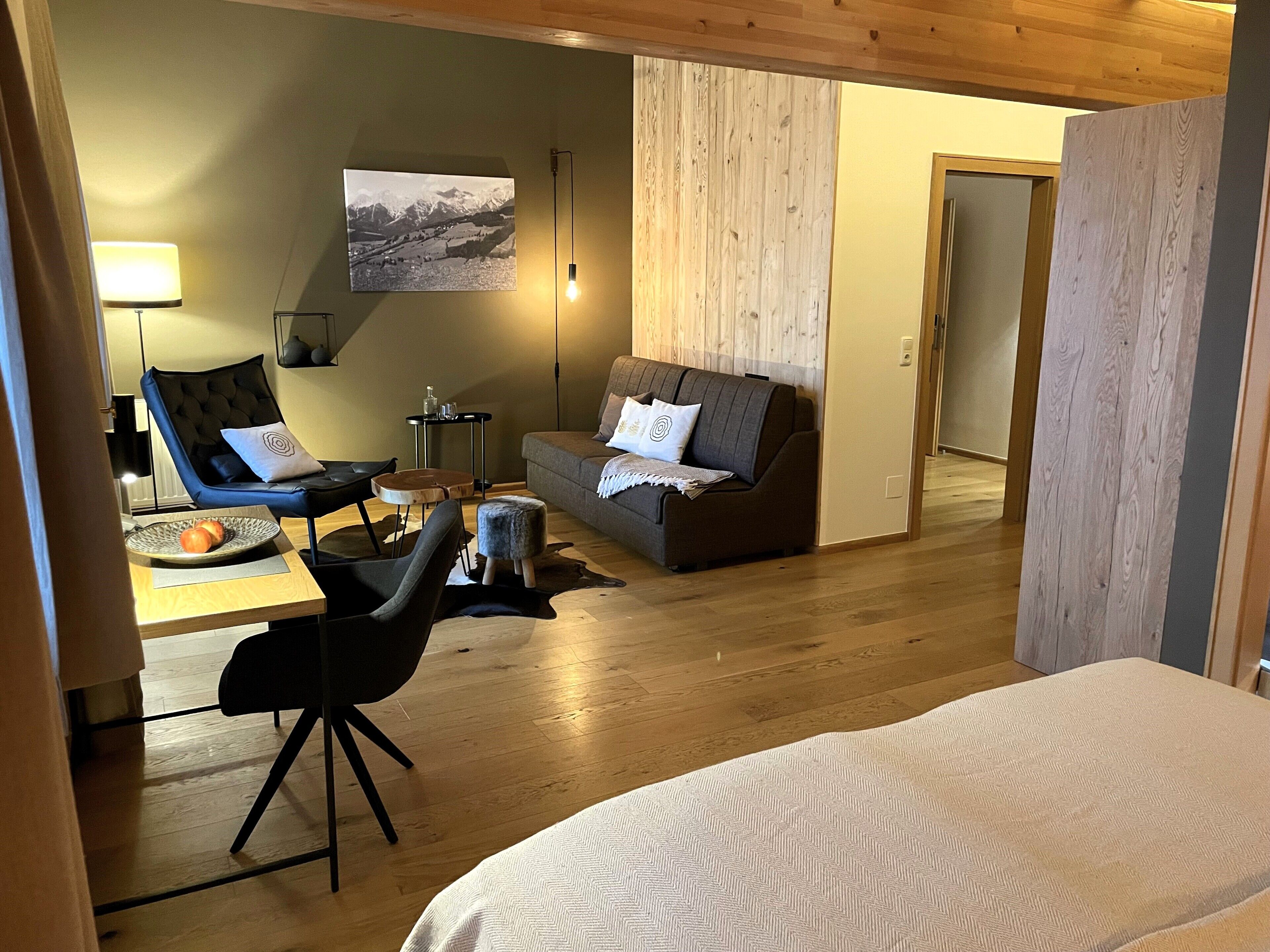 Una habitación acogedora con cama, sofá, sillón, mesita y lámpara.