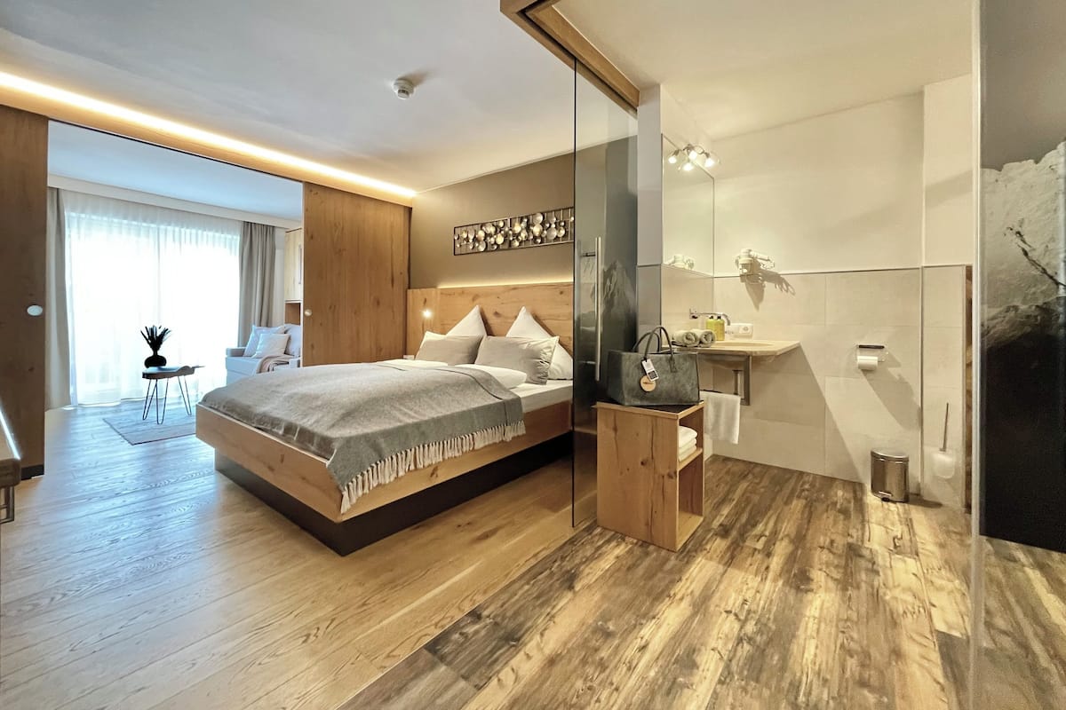 Ein modernes Schlafzimmer mit einem großen Bett, Holzboden, einer Glasdusche und Blick ins Freie.