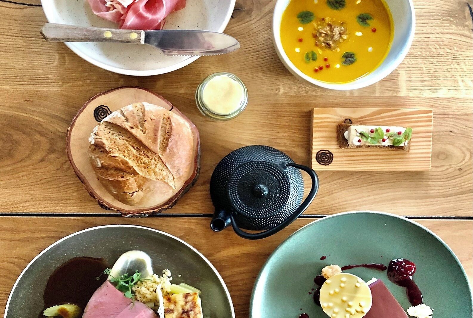 A wooden table with various dishes including bread, soup, and desserts.