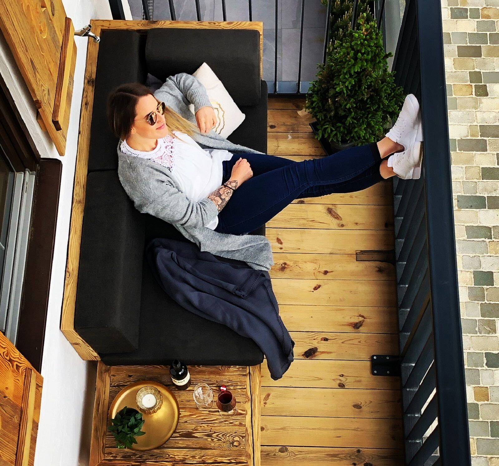 A person lying on a black sofa in a room with wooden flooring and a brick wall.