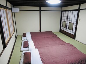 A traditional Japanese-style room with tatami flooring, a low bed with a red and white bedspread, and shoji screens on the walls.