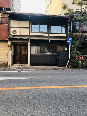 A two-story building with a black and beige facade, a gated entrance, and a blue directional sign.