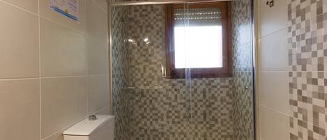 Un baño con cabina de ducha, inodoro y ventana.