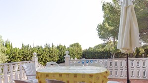 Eine Terrasse im Freien mit einem runden Tisch und Stühlen, umgeben von einem weißen Zaun und Pflanzen.
