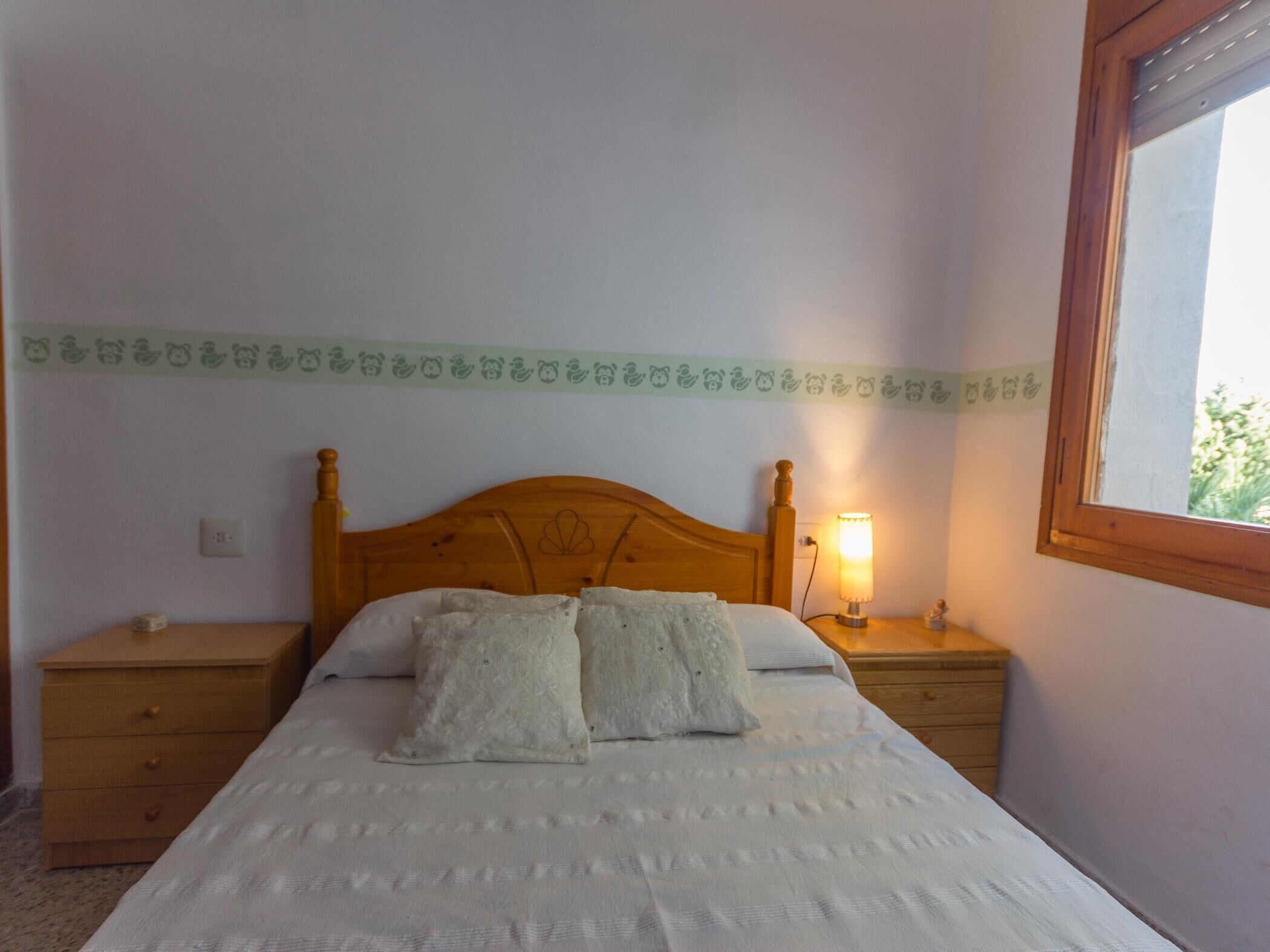 Een slaapkamer met een houten bed, twee nachtkastjes, een lamp en een raam.