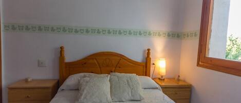 Een slaapkamer met een houten bed, twee nachtkastjes, een lamp en een raam.