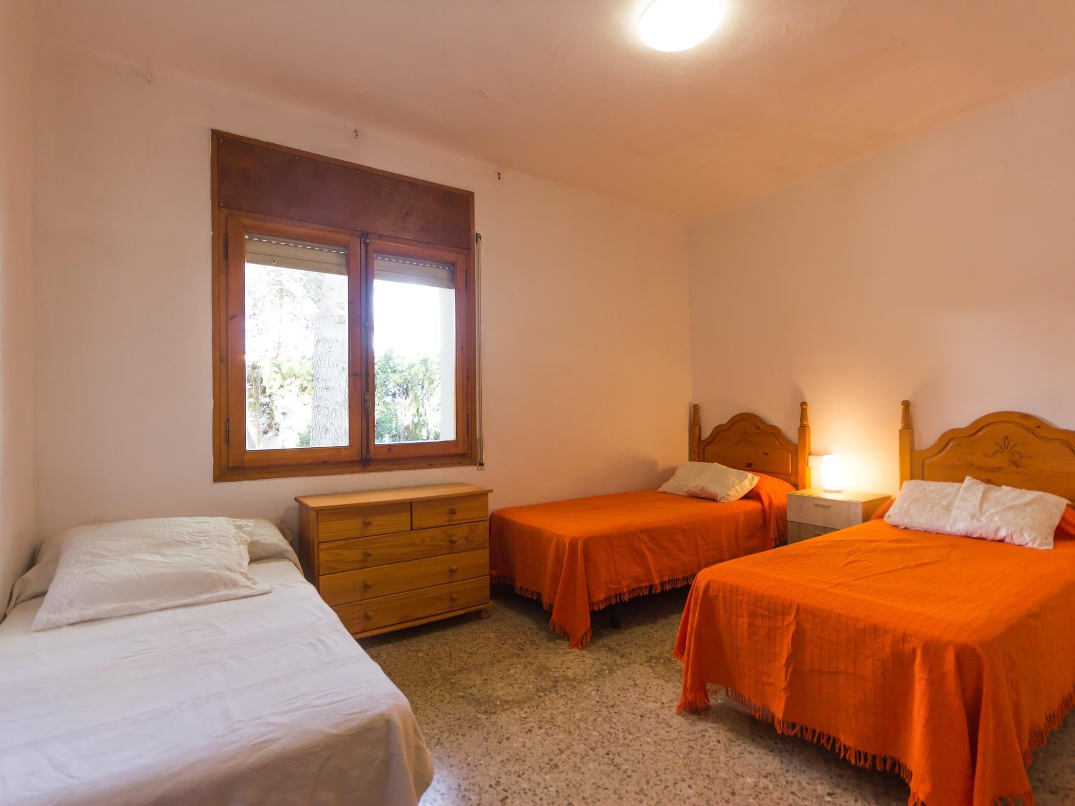 Quarto com duas camas de solteiro, cômoda de madeira e janela com cortinas.