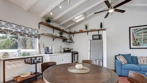 A modern kitchen with white cabinets, a wooden dining table, and a blue sofa in the living area.
