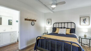 A bedroom with a bed, bedside tables, a ceiling fan, and artwork on the walls.