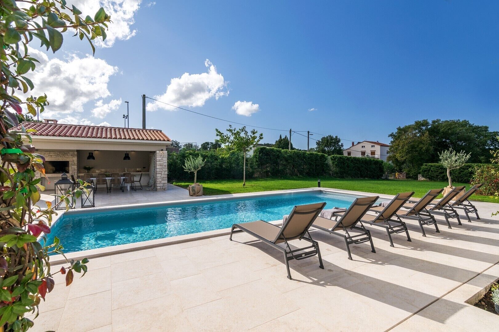 Una piscina amb gandules, una zona de terrassa i vista cap a una casa al fons.