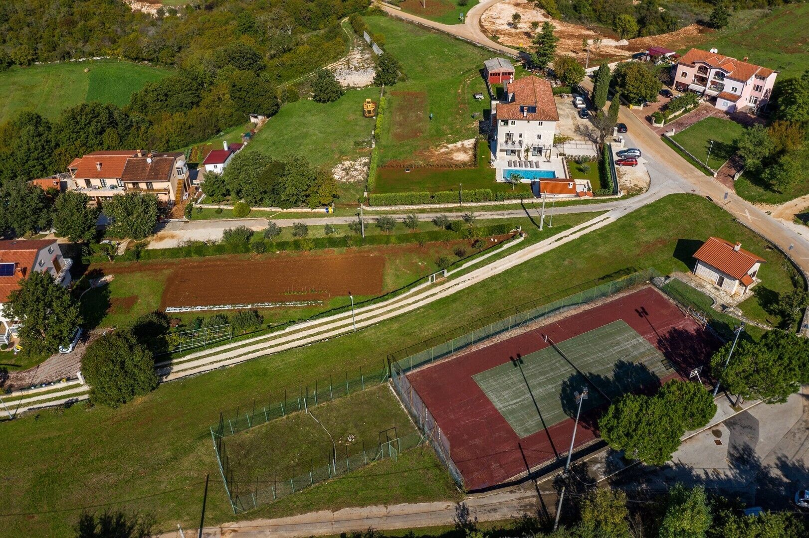 An aerial view of a residential area with houses, a sports field, and a tennis court.