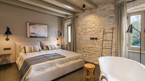 Een slaapkamer met een groot bed, een stenen muur, een raam met gordijnen en een bad.