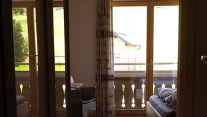 A room with a wooden floor, a sofa, a chair, a table, and a window with curtains. - Hotel Sonnenlicht (Maria Alm am Steinernen Meer)