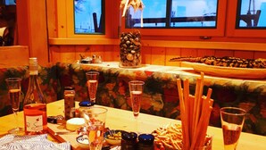 A dining table set with various food items, glasses, and utensils, with a window view of a snowy landscape. - Hotel Sonnenlicht (Maria Alm am Steinernen Meer)