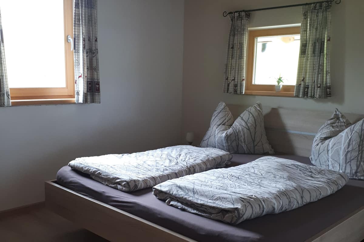 A bedroom with a wooden bed frame, two beds, and a window with curtains.
