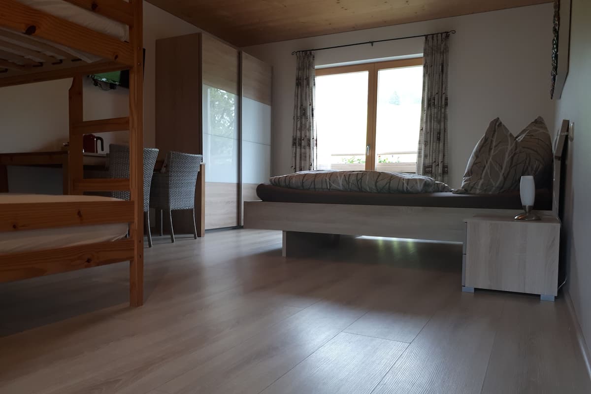 A room with a bunk bed, a sofa bed, a small table, and a chair.