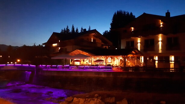 A large building with a covered outdoor area, stone walls, and a water feature. - Hotel Sonnenlicht (Maria Alm am Steinernen Meer)