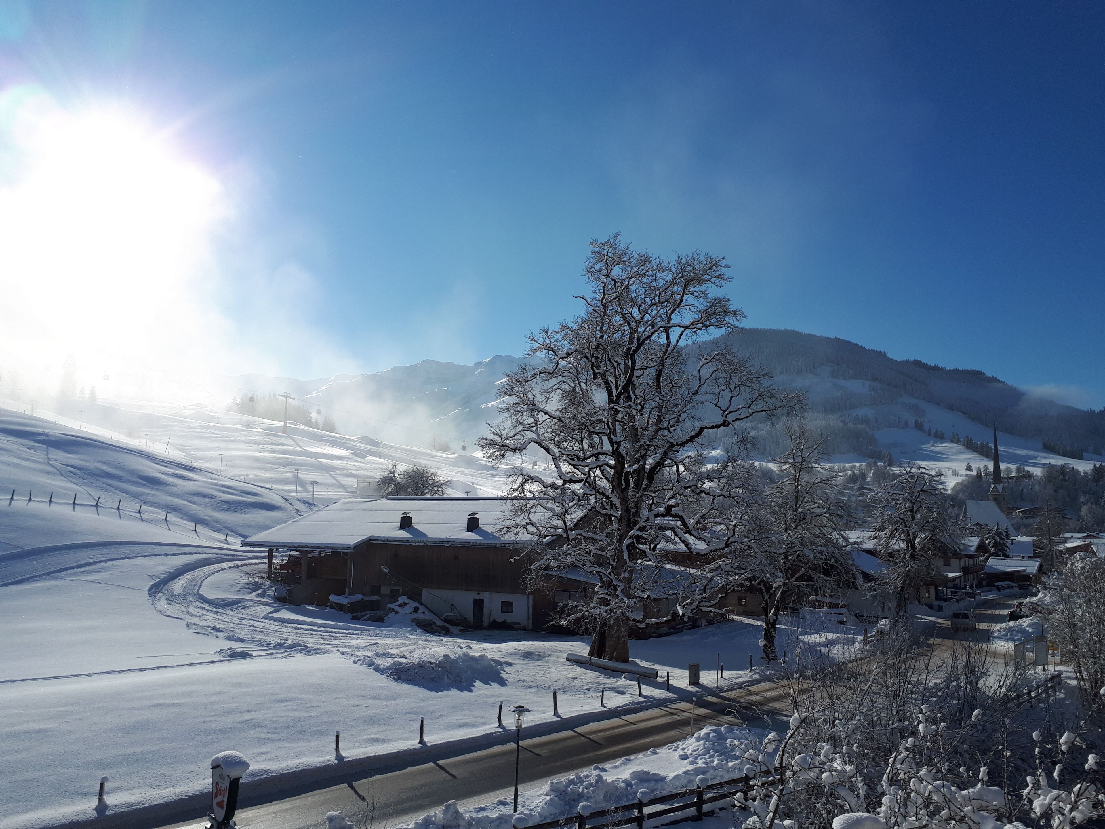 A snow-covered landscape with a clear sky, a road, and buildings in the distance.