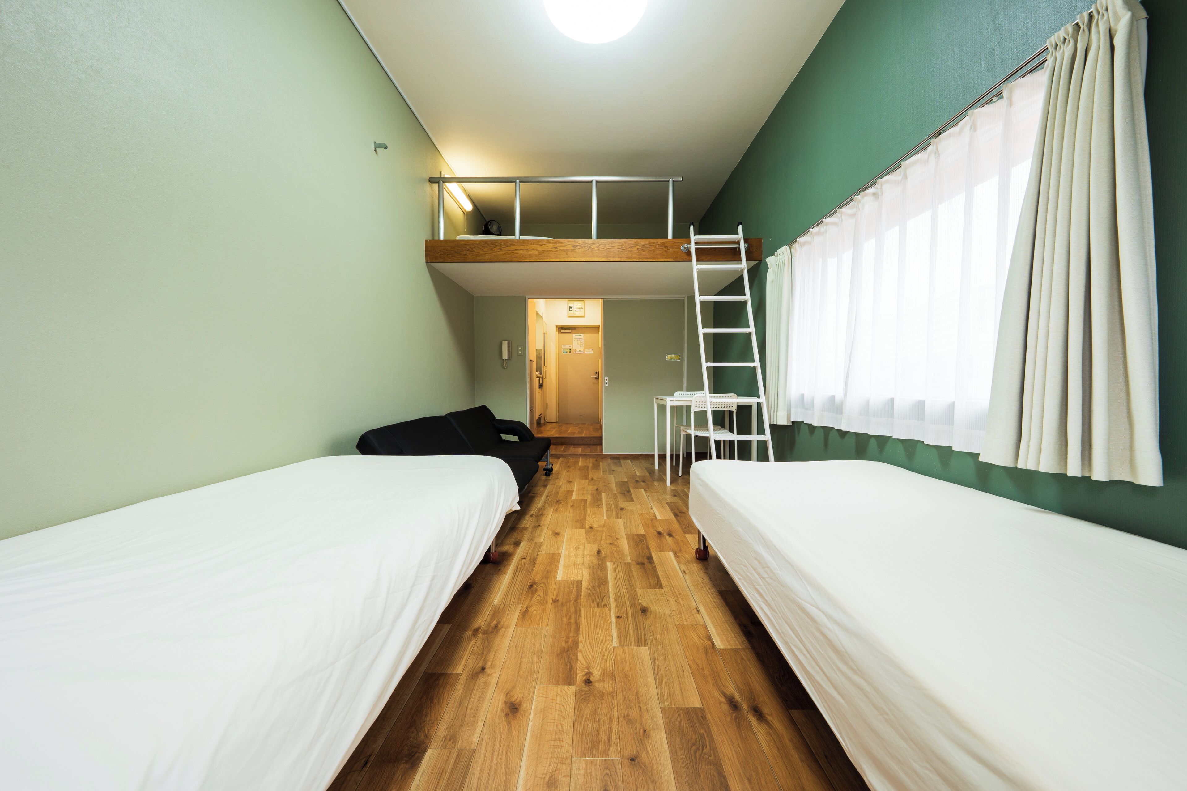 Habitación tipo dormitorio con dos camas, una cama elevada, suelo de madera, cortina blanca y una silla blanca.