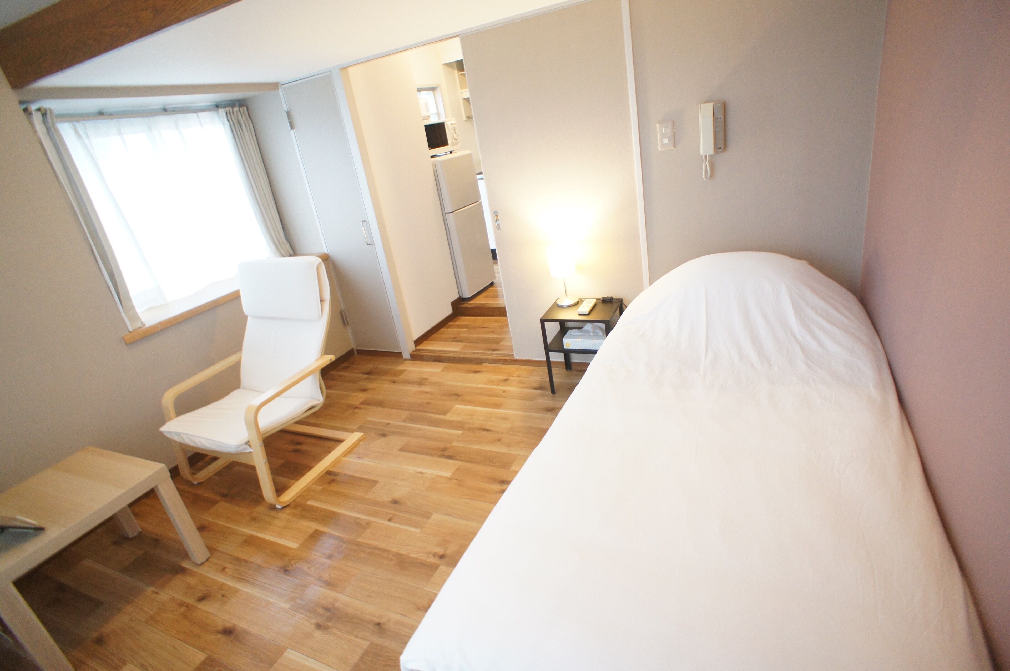 Una habitación pequeña con cama, una silla, una mesita y una ventana.